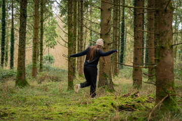 middle-aged white woman with brown hair, wearing a black sweater and a beige hat, in an Irish winter forest.