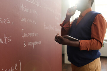 Closeup of senior African American college professor writing on chalkboard while preparing for...