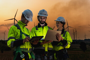 Fototapeta premium Modern expertise wind turbine engineer team with notebook working at windmill farm at sunset