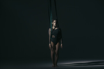 Portrait of two female acrobats in studio isolated on black background. Girls aerial dancers performing element with ropes.