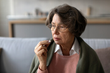 Upset senior ill woman holding pill, taking painkiller medicine to relieve headache pain, lady...
