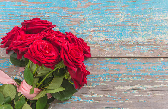 Bouquet of red roses flowers with pink ribbon on a old blue paint wooden background; Valentines day greeting card concept
