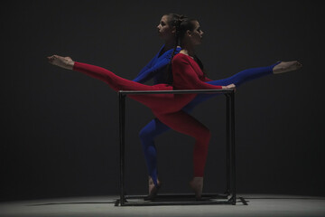 Portrait of two female acrobats isolated on black background. Girls aerial dancers in blue red...
