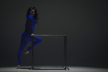 Portrait of female acrobat isolated on black background. Woman gymnastic dancer in blue sparkling bodysuit showing element on a cube.