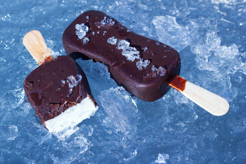 The classic milky ice cream with chocolate glaze on wooden stick. The sweet frozen dessert on the natural chopped ice. Closeup view. - 723966269