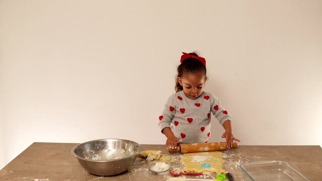 Ni&ntilde;a feliz amasando con rodillo la masa para hacer galletas para compartir en el d&iacute;a de San Valent&iacute;n amor y amistad preparando y aprendiendo a cocinar jugando y divertida