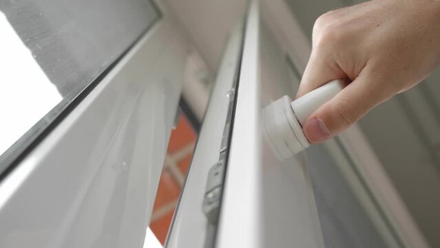 A close-up of a man's hand turns the handle of the window frame and opens a PVC plastic window, letting fresh air into the room and changing the temperature and humidity in the room.