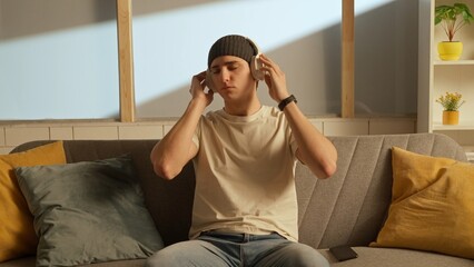 Fototapeta premium Portrait of young person in the room sitting on the couch. Man in headphones listening to music.