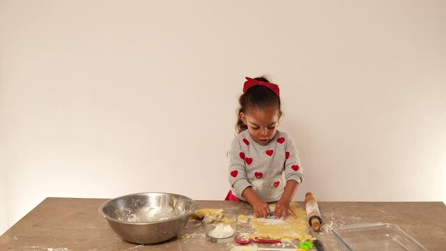 Ni&ntilde;a feliz latina amasando con rodillo y cortando la masa para hacer galletas para compartir con su familia en el d&iacute;a de San Valent&iacute;n amor y amistad preparando y aprendiendo a cocinar 