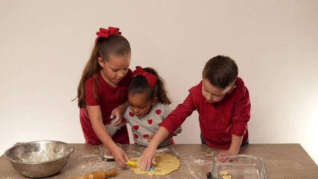 tres ni&ntilde;os hermanos latinos divertidos preparando galletas caseras para compartir con ingredientes y utensilios de reposter&iacute;a