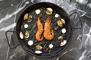 Spanish paella with black rice and seafood in traditional pan