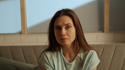 Portrait of young person in the room sitting on the couch. Woman sitting on the sofa looks at camera directly, tears in eyes, sad mood upset expression.