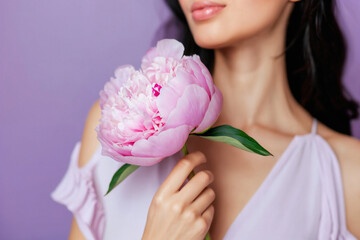 A sophisticated image of a woman in a white dress holding a lush pink peony near her face, set against a soft purple background, illustrating grace and femininity