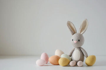 A soft, plush bunny toy displayed alongside a collection of multicolored pastel Easter eggs on a clean white background