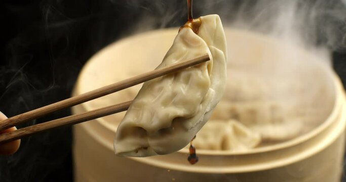 Super slow motion of organic soy sauce dripping on steamed homemade asian traditional recipe fresh pasta gyoza stuffed with meat kept with bamboo chopsticks in japanese chinese restaurant at 1000 fps.