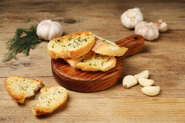 Tasty baguette with garlic and dill on wooden table
