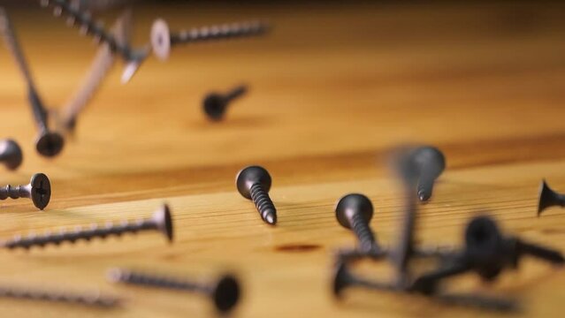Metal self-tapping screws spill out onto a wooden tabletop. Make wooden products. Start repair or construction. Building materials and bolts and nails.