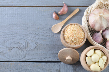 Dehydrated garlic granules and fresh bulbs on grey wooden table, flat lay. Space for text