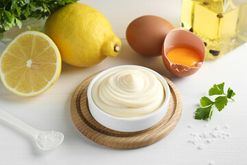 Fresh mayonnaise sauce in bowl and ingredients on white wooden table