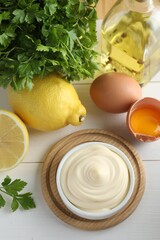 Fresh mayonnaise sauce in bowl and ingredients on white wooden table, flat lay