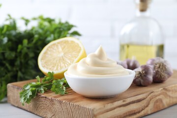 Tasty mayonnaise sauce in bowl, parsley, garlic and lemon on table, closeup