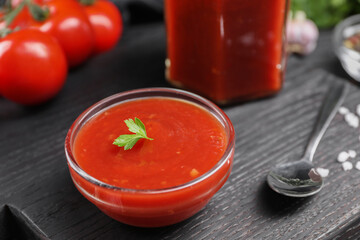 Delicious ketchup, parsley and spoon on black wooden board, closeup. Tomato sauce