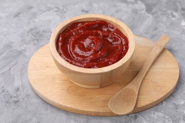 Organic ketchup in wooden bowl and spoon on grey textured table. Tomato sauce