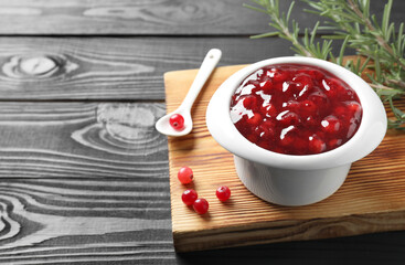 Cranberry sauce in bowl, fresh berries, spoon and rosemary on black wooden table, closeup. Space for text