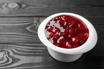 Fresh cranberry sauce in bowl on black wooden table, closeup. Space for text