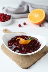 Fresh cranberry sauce, orange peel and rosemary in bowl on white wooden table, closeup