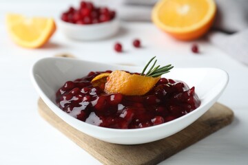Fresh cranberry sauce, orange peel and rosemary in bowl on white table, closeup