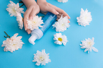 Flat lay Woman hands with bottle with water foam for cleansing on blue background with white flowers. Concept natural cosmetics for facial skin care