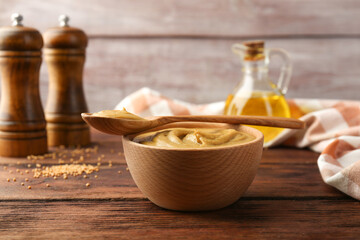Bowl and spoon with tasty mustard sauce on wooden table
