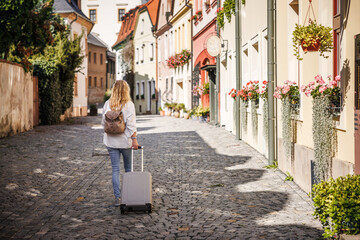 Solo travel. Woman tourist with suitcase and backpack walking on street. Traveling and vacation in european city Olomouc, Czech Republic - obrazy, fototapety, plakaty