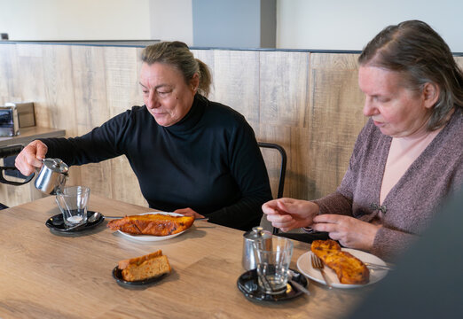 Two elderly friends in a cafeteria eating torrijas and tea