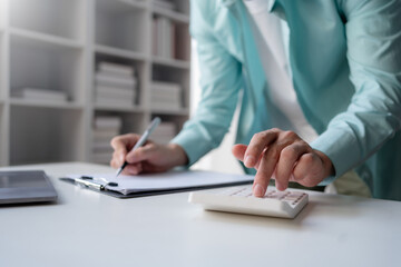 Business professional using a calculator and taking notes, financial planning or budgeting on a clipboard in an office.