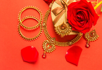 Classic design of an Indian gold necklace and bangles set arranged with heart shap gift box and red rose flowers.