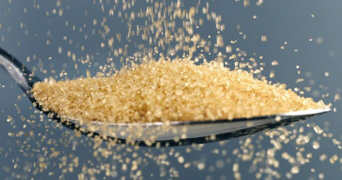 Super slow motion macro of sweet refined granulated brown sugar is falling with crystal grains on silver spoon isolated on soft background at 1000 fps.