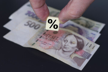 Fingers holding a plastic element with a percent sign on the background of Czech crown banknotes.