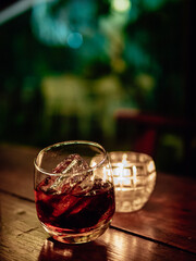 Dramatic top view of a glass of whiskey with ice cubes on wooden background. A glass of whiskey is placed on the counter inside the bar with back lighting. tumbler of whiskey brandy and ice