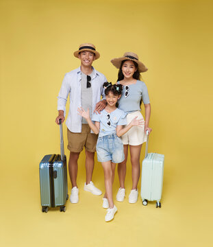 Happy fun asian family vacation portrait. Father, mother and daughters ready for travel flight with suitcase isolated on yellow studio background.