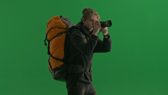 Side view of a male traveler taking a photo with a camera while hiking. Man hiker walking in studio on green screen close up. Concept of travel, active rest, hiking.