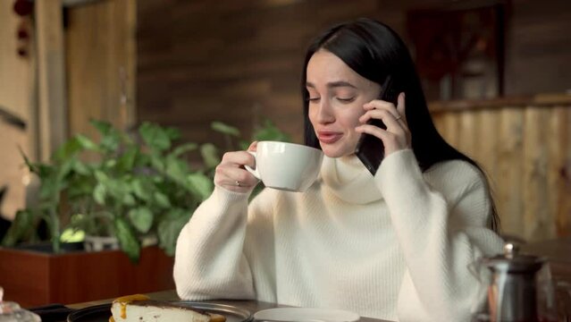Happy girl calling with friends on smartphone while spending time at cafe drinking coffee