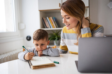 Happy mother with laptop helping son with homework at home