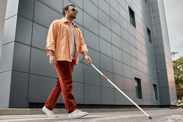 glad indian blind man in orange jacket with walking stick and glasses with gray wall on backdrop