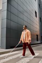 joyful indian blind man in orange jacket with walking stick and glasses with gray wall on backdrop