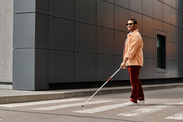 joyous indian blind man in orange jacket with walking stick and glasses with gray wall on backdrop