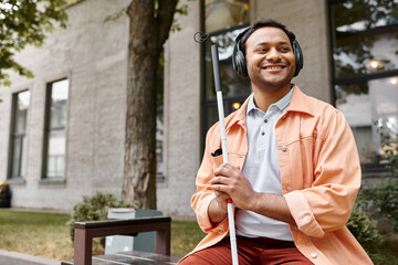 jolly indian man with blindness in headphones with walking stick enjoying music while outside