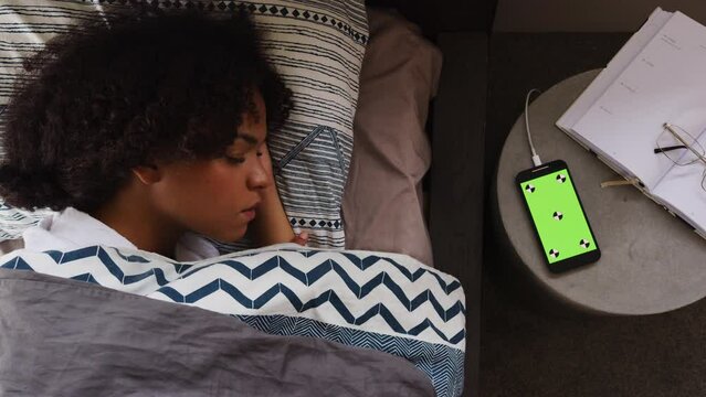 A Phone with a green screen on the table next to a sleeping woman
