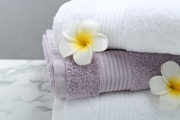 Stack of folded terry towels and plumeria flowers on white marble table, closeup
